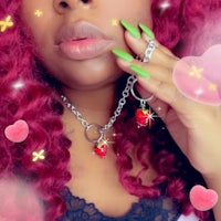 a woman with red hair and pink nails holding a strawberry necklace